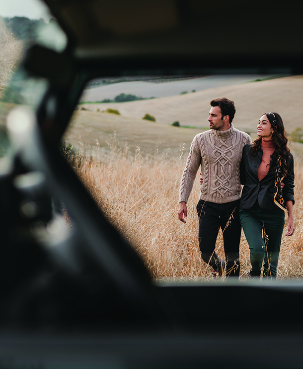 Couple walking in Tuscany countryside seen through window of Defender