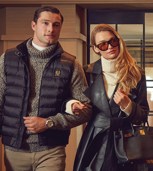 Man wearing vest and sweater with woman wearing black leather coat, sunglasses, and black handbag