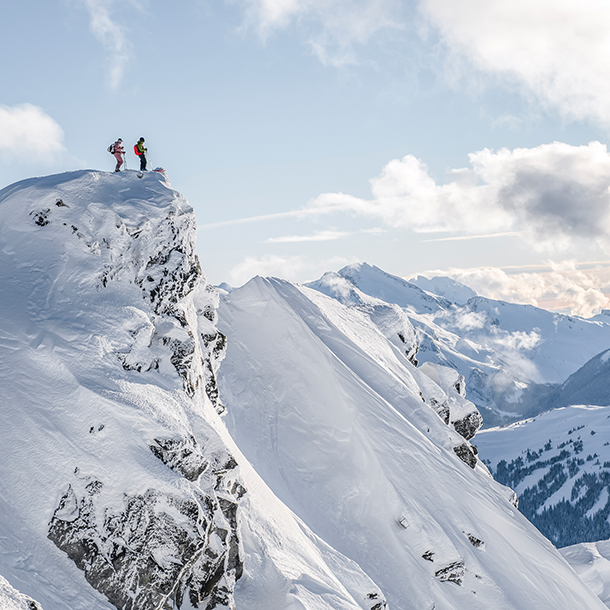 Two mountain climbers standing at the mountain peak gazing at the breathtaking view below.