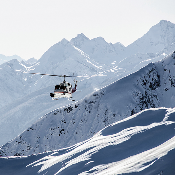 A heli-ski helicopter is flying over a snow-covered mountain range.  Caption: Heli-skiing in British Columbia, Canada