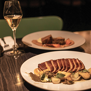 Two plates of food and a glass of white wine on a restaurant table