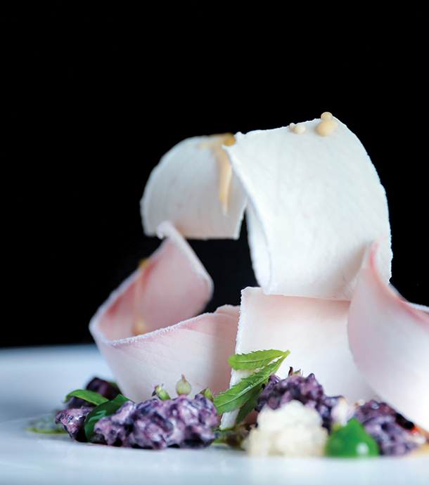 An elegant and carefully plated dish of thinly sliced, curled Hamachi, black rice, finger limes and mint. 