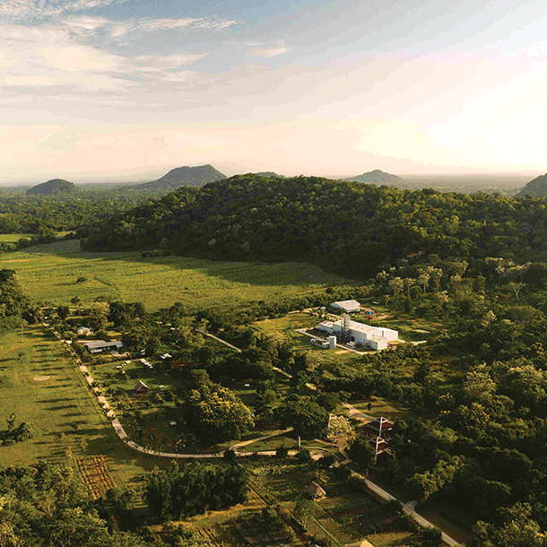 Aerial view of a lush green valley with a farm, road and white distillery building in the center. There are mountains in the background.