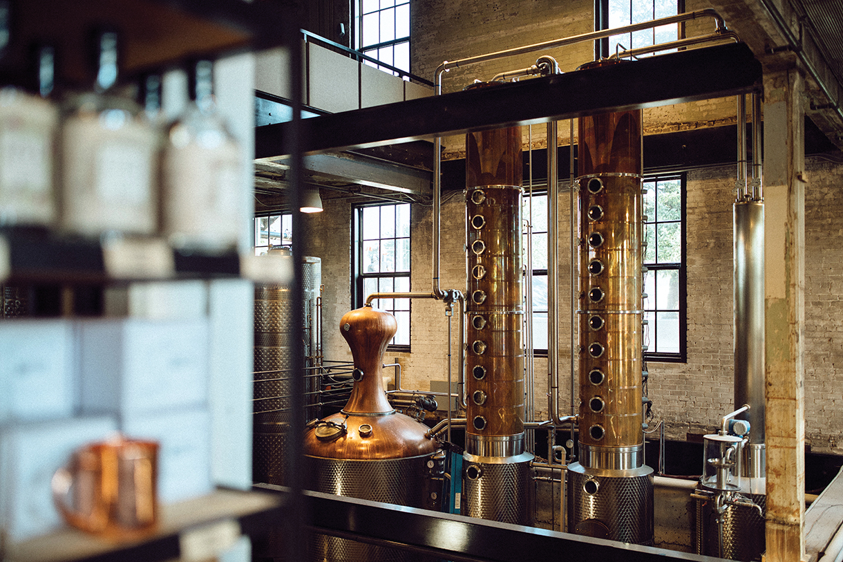 Copper distillery equipment inside a large industrial building. The equipment consists of several interconnected pipes and tanks.