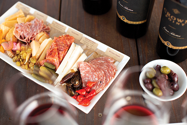 An assortment of salami, cheese, olives, and wines on a dark wooden table.