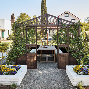 Outdoor gazebo with table and chairs located in the middle of a garden.