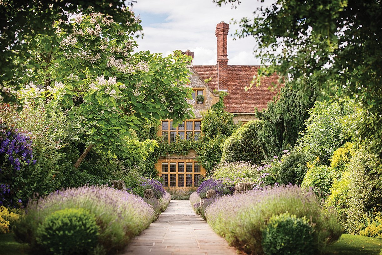 A house with windows surrounded by a lush wildflower garden with a path leading to it