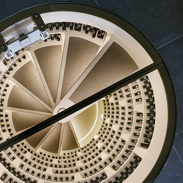 A below-ground wine cellar with wooden shelves stocked with bottles of wine. There is a spiral staircase with wrought iron railings that leads down into the wine cellar. Caption: Below-ground Spiral Cellar in London