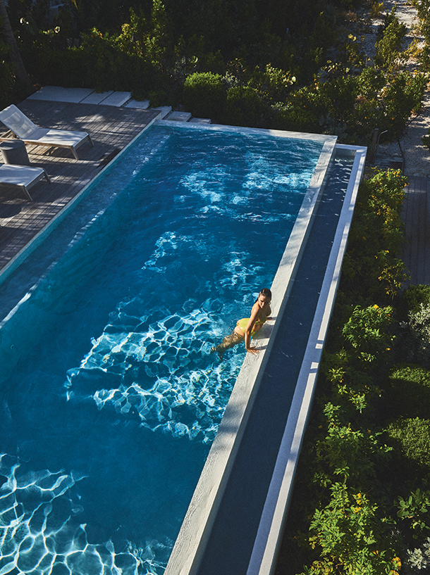 Woman in yellow sparkle bikini standing in infinity pool looking out