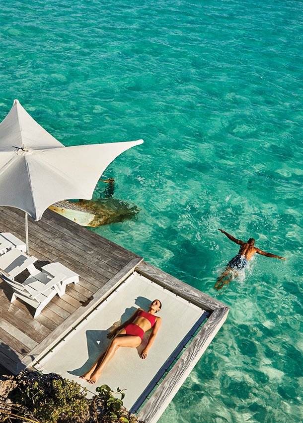 Woman relaxing on deck above water and a man swimming in the ocean at one of Wymara’s private residences