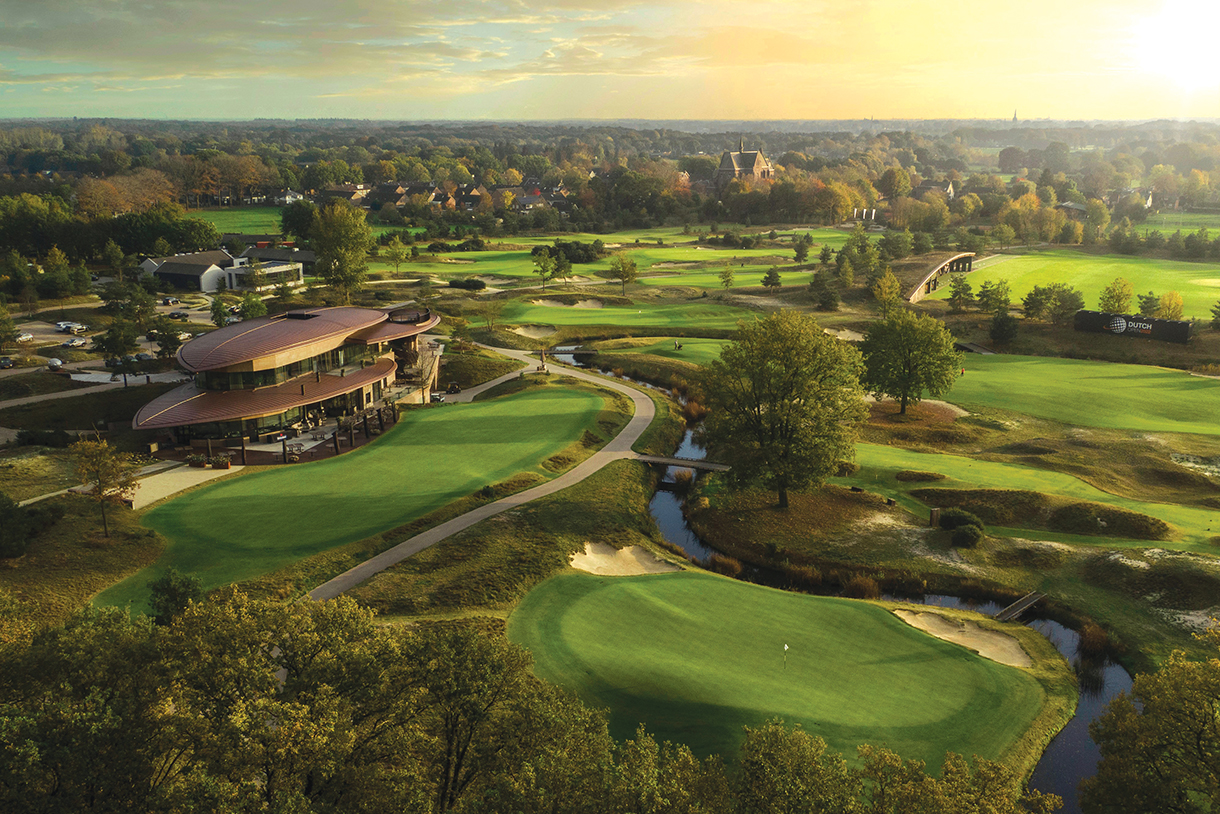 Modern clubhouse surrounded by heathland-styled golf course with scattered greens and bunkers that blend in with the background of water and greenery.