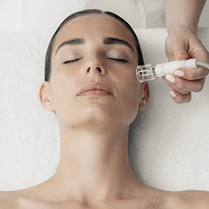 Woman laying face up receiving facial treatment with specialized facial device