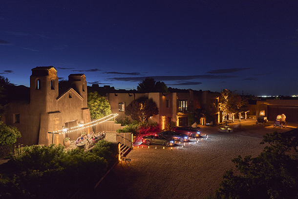 Outdoor private dining experience under the night sky at a Western adobe property with parked Bentleys, stagecoaches, and a chuck wagon parked outside 