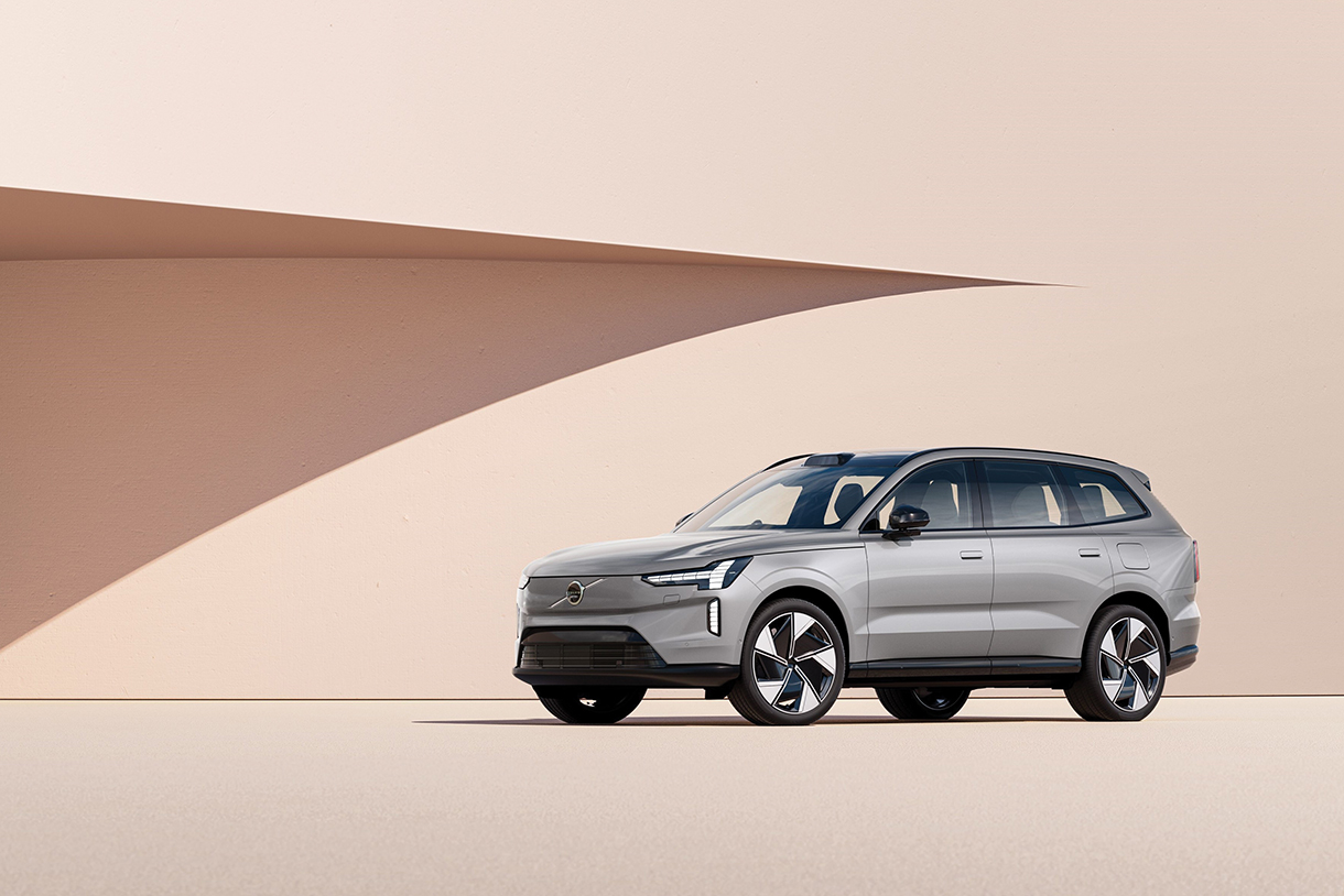 Side view of silver 2024 Volvo EX90 parked in front of a contemporary light peach-colored building 