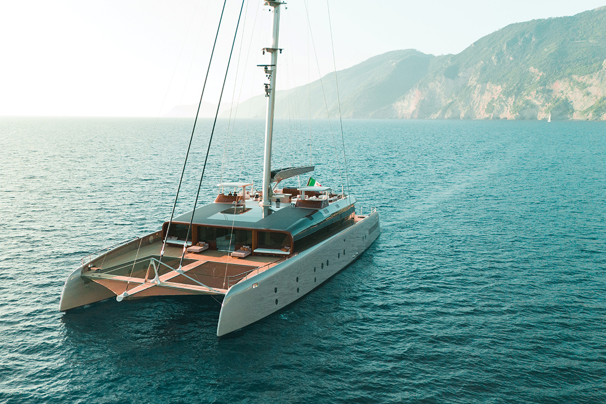 Aerial view of a large, modern catamaran yacht named ArtExplorer. The yacht is designed for luxury and sustainability, with a focus on environmental responsibility. It has a sleek and modern design with a spacious deck and plenty of outdoor living space.