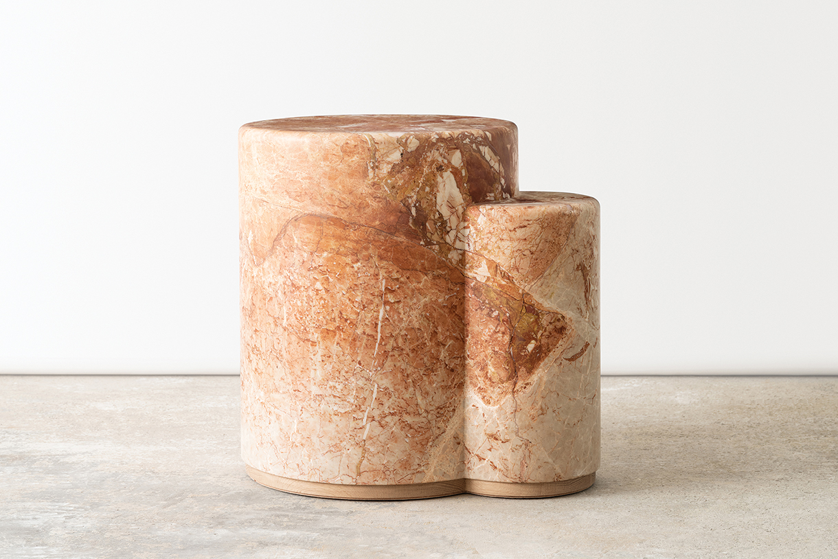 A small, cylindrical side table made of brown marble with a textured surface. A smaller, cylindrical piece is attached to the side of the larger one, creating a unique, sculptural shape. 