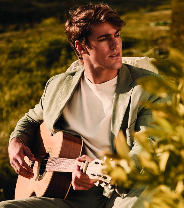 Man wearing a white sweater with jacket playing a guitar