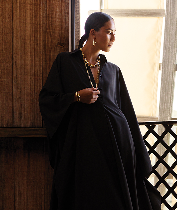 Woman with black button-down dress wearing layers of gold jewelry.