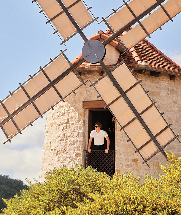 Man wearing white polo shirt, dark pants and sunglasses standing inside of an old fashioned brick windmill.