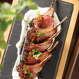 Closeup of a lamb chops entrée on a dark gray serving dish