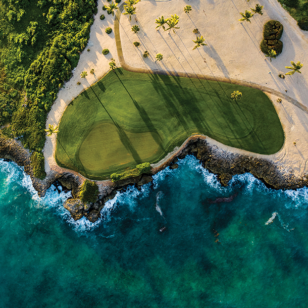 An aerial view of  beautiful green golf course with sand traps surrounded by blue ocean