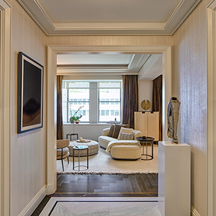 A brightly lit hallway with hardwood floors leads into a spacious living room. A white statue rests on a black pedestal in the hallway.