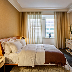  A casual standard bedroom with yellow walls, curtains, white ceiling, a bed, dresser and window. There is a view of a building from the window.