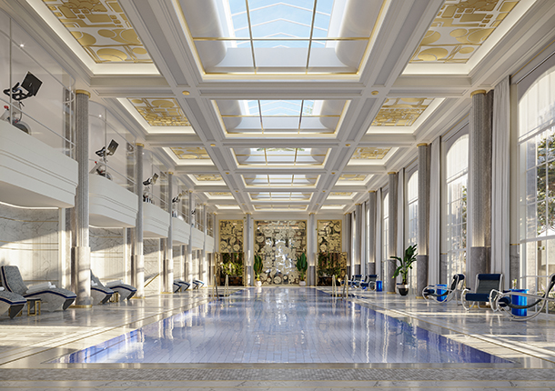 A large luxurious indoor swimming pool with a skylight in the ceiling. There is a gym on the second floor that overlooks the pool and several lounge chairs on the pool deck surrounding the pool.