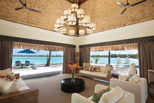 An interior view of a luxurious living room of a villa at an island resort. The room opens up to a beautiful private beach and view of the ocean.