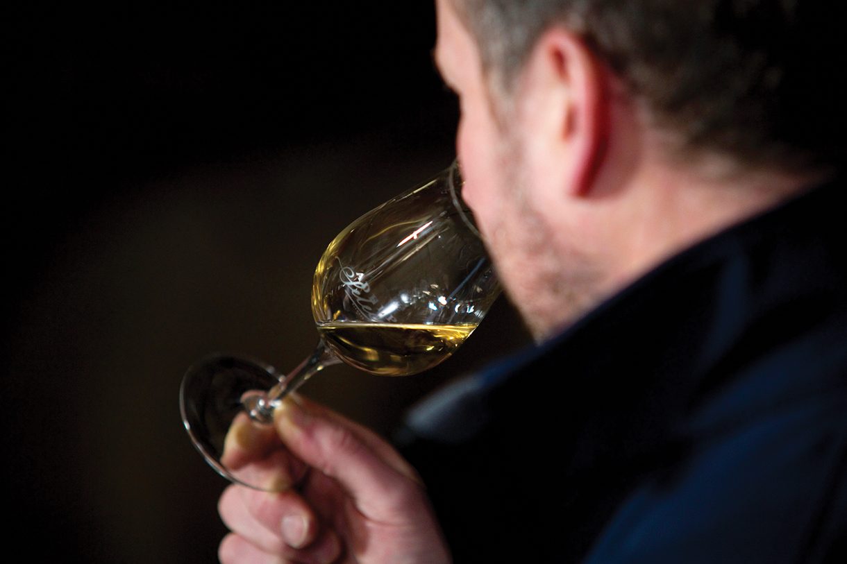 Side view of a man wearing a black shirt drinking a glass of whisky. The glass he is holding has a logo on it that reads Adephi Select.