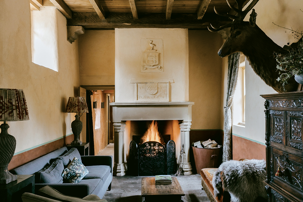 Cozy living room with a fireplace, featuring a stone mantle, a deer head mount, and antique furniture.