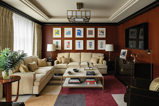 A beautiful living room with a burgundy wall, a cream-colored sofa, and a coffee table filled with books and decorative items. There is a gallery wall of framed artwork above the sofa.