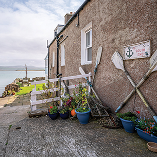 A closeup of the side of a house on the coast of Kirkwall in the Orkney Islands. There is a small boat in the water behind the house.