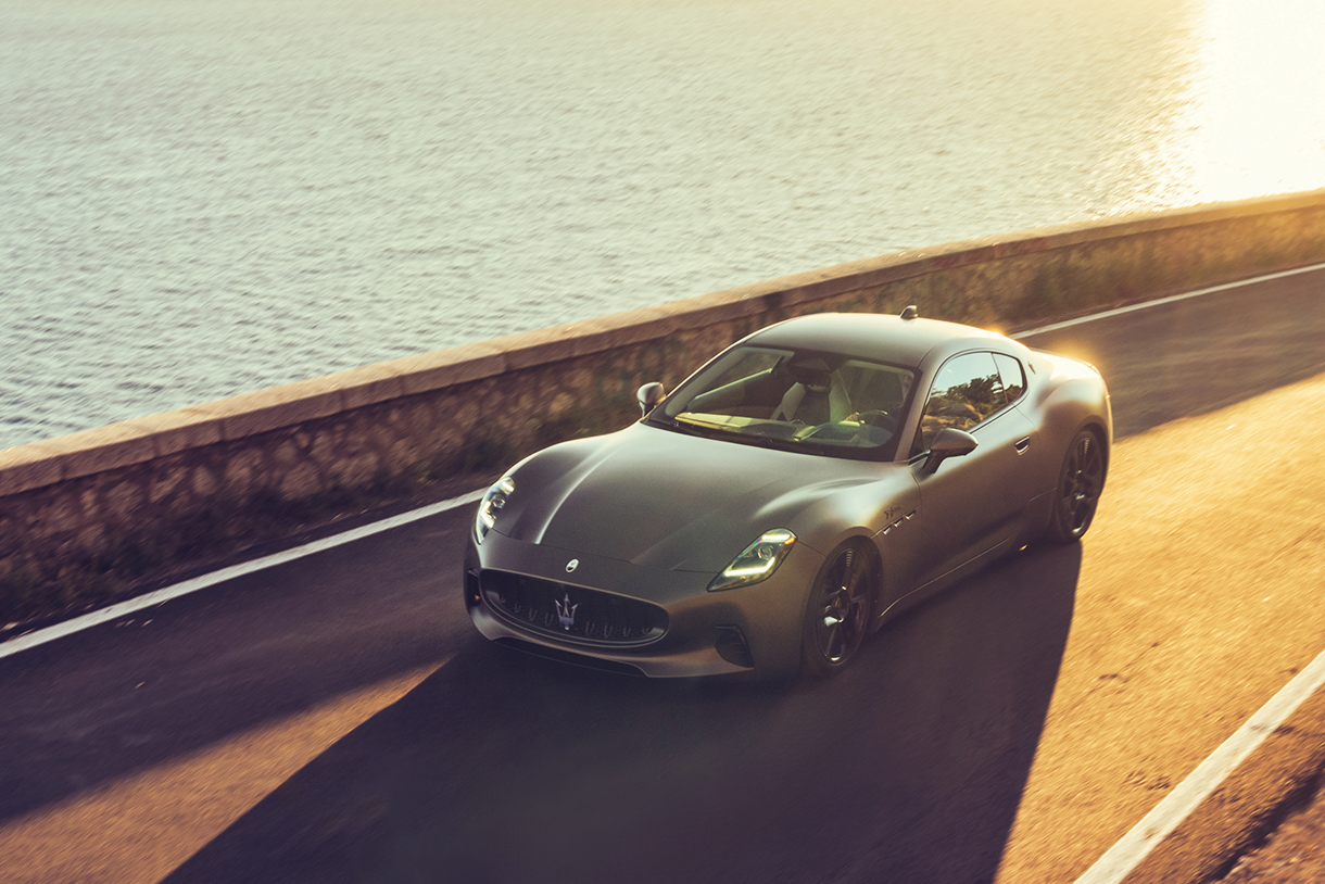 A front overhead view of a dark silver gray Maserati GranTurismo Folgore driving on a coastal road