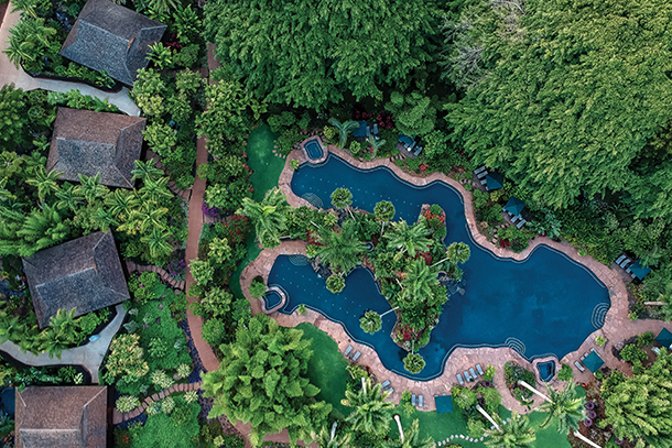 An aerial view of Sensei Lanai, showcasing a winding pool surrounded by lush tropical vegetation. The resort's buildings are nestled amidst the greenery, creating a serene and secluded atmosphere.