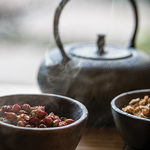 A close-up of a traditional Japanese teapot and bowls filled with dried rosebuds and other tea leaves, ready for a tea ceremony.