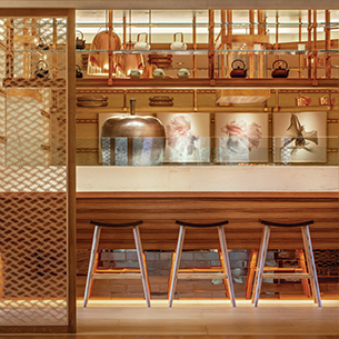 A sleek and modern Japanese restaurant interior, featuring a wooden bar with high-top stools, a glass display case showcasing traditional Japanese ceramics, and a minimalist design aesthetic.