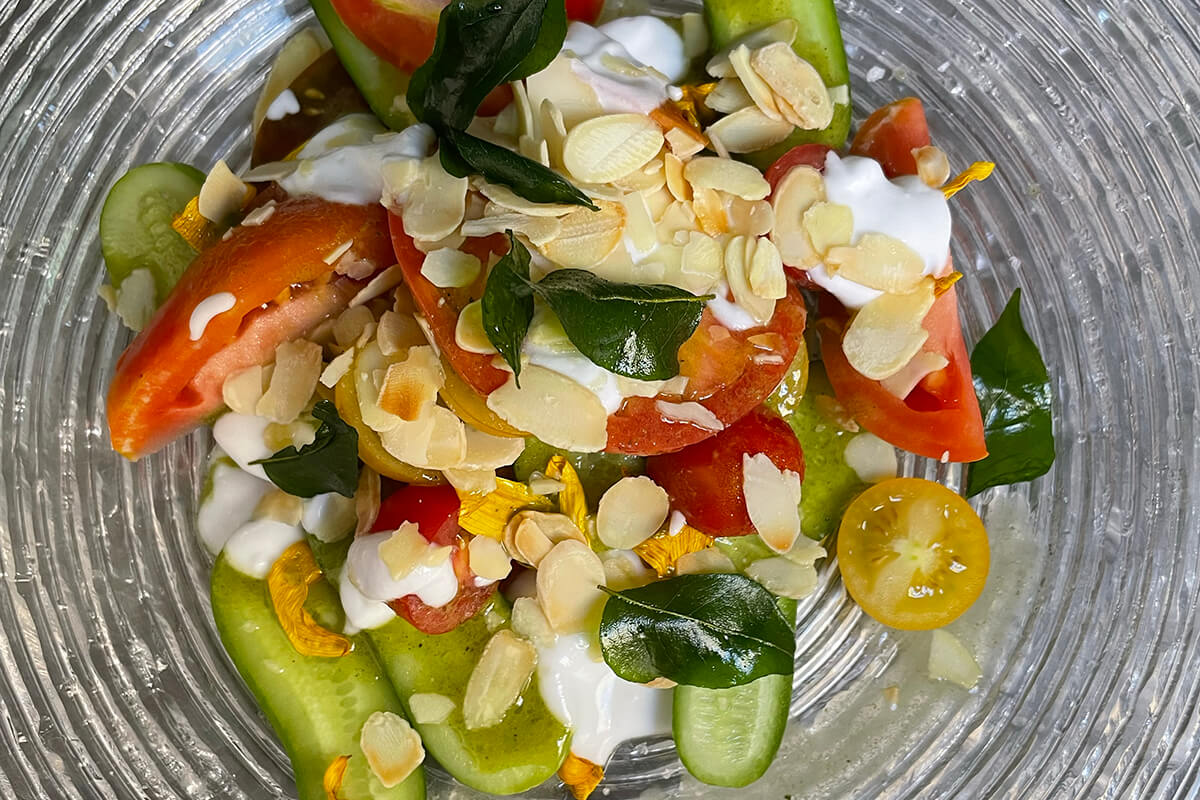 A colorful and vibrant display of fresh produce from South Africa. The items include ripe red tomatoes, small green eugenia berries, and orange sea pumpkins arranged on a plate.