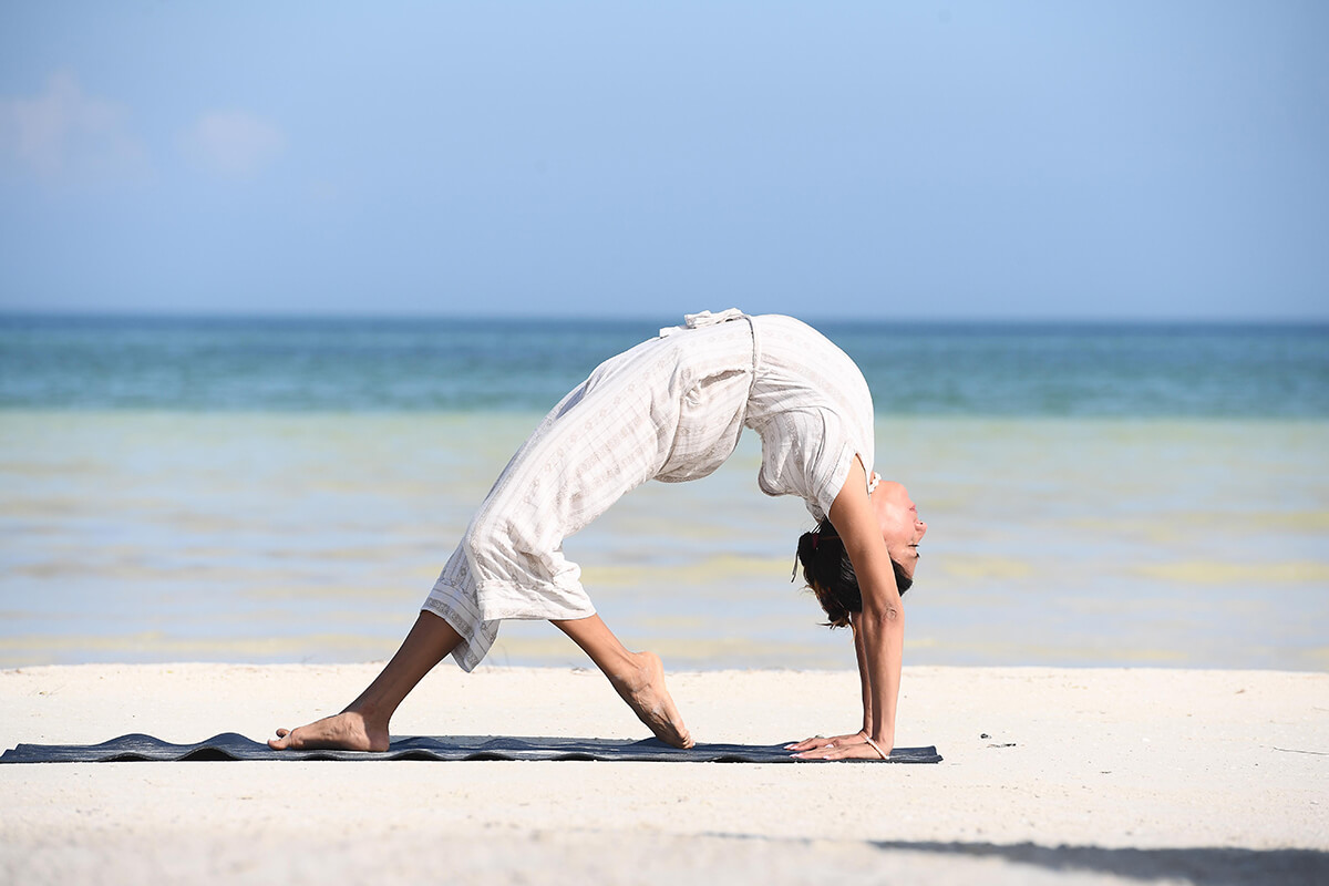 A serene beach setting at Casa Sandra on the island of Holbox in Mexico. The image shows a woman doing yoga on a mat laid out on the sand with the ocean behind her. 